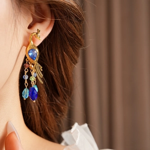 Detail of vintage gold peacock earrings with blue gemstones and colorful beaded tassels