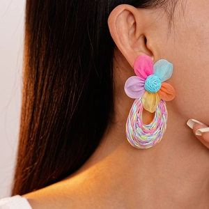 Close-up of handmade lace flower raffia earrings featuring colorful woven details on model