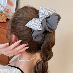 Close-up of a grey scrunchie with a black and white grid pattern bow on a brown braid