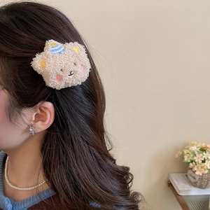 Detail view of a cute beige plush bear hair claw clip worn by a model in a cozy setting