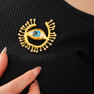 Close-up of vintage gold evil eye brooch with blue resin and zircon rays on black fabric