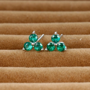 Macro shot of clover-shaped stud earrings featuring three round-cut emerald green gemstones