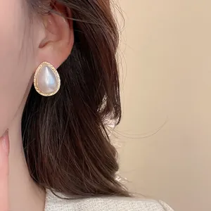 Elegant water drop pearl stud earrings with gold textured edges worn by a female model
