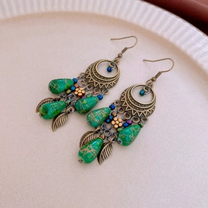Macro detail of Bohemian leaf drop tassel earrings with green turquoise-style beads