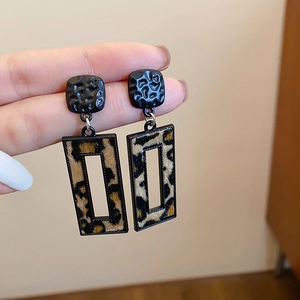 Detail of square black textured earrings with a hollow frame and leopard print inlay