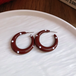 Close-up of C-shaped resin earrings with white polka dots on a deep red glossy surface