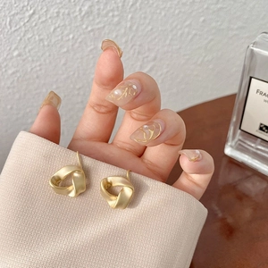 Detail of twisted geometric gold clip-on earrings held against a soft beige background
