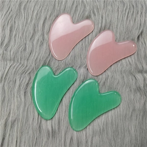 Pink and green heart-shaped jade gua sha scraping tools on a soft grey plush surface