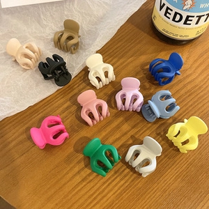 Flat lay of thirteen colorful matte plastic hair claw clips on a rustic wooden table
