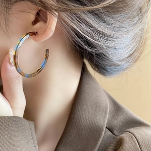 Detail of C-shaped resin hoop earrings with vintage tortoiseshell and blue color splicing