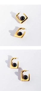 Detailed view of geometric square gold earrings with black bead inlays on white background