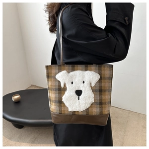 Detail of plaid tote bag featuring a cute plush dog patch and brown leather handles