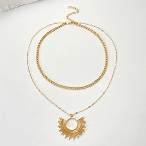 Détail du collier double couche doré avec pendentif soleil et fermoir mousqueton sur marbre