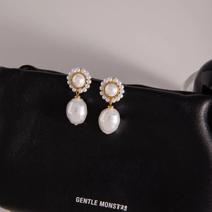 Detail of baroque pearl drop earrings with gold floral cluster stud on black leather