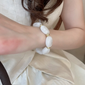 Detail of acrylic oval beads with marble texture and golden spacers on the wrist