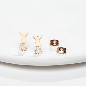 Macro shot of minimalist dog silhouette earrings in rose gold on a ceramic base