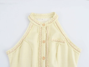 Détail de la texture en tweed avec boutons dorés et étiquette taille S sur robe jaune sans manches