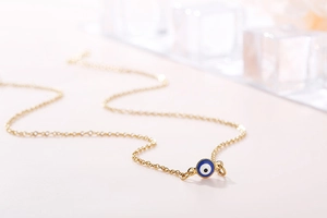Detail of gold evil eye pendant necklace with blue enamel on a minimalist background