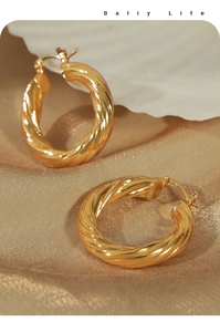 Close-up of golden hoop earrings with intricate twisted rope texture on silk background