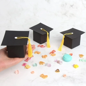 Miniature black graduation cap favor box with yellow tassel held in hand for scale