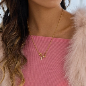 Close-up of golden paperclip necklace with cross and heart charms on model