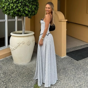 Detail of white polka dot maxi dress featuring black lace trim and pleated chiffon fabric