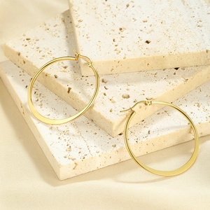 Detail of matte gold circular hoop earrings placed on a textured stone surface
