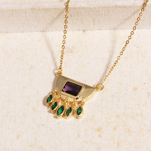 Detailed shot of golden necklace with purple rectangular stone and green teardrop gems