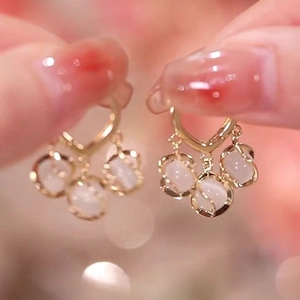 Close-up of golden heart earrings featuring three dangling milky cat-eye stone pendants