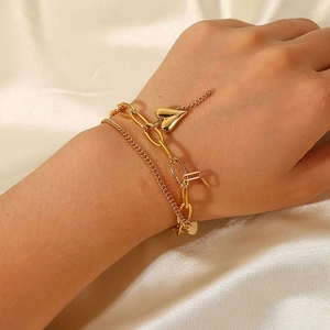 Detailed view of layered gold heart bracelet on wrist with satin fabric background