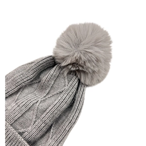 Gros plan du bonnet gris en maille torsadée avec un pompon en fausse fourrure douce