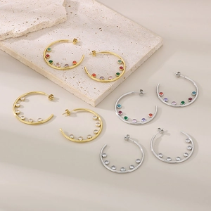 Detailed shot of C-shaped stainless steel earrings with colorful zircons on stone base
