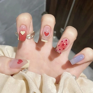 Detailed close-up of glossy press-on nails featuring red hearts, pearls and 3D accents