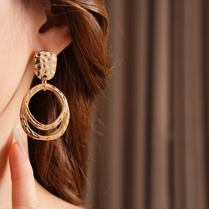 Detail of golden double-hoop earrings with hammered texture worn by a model