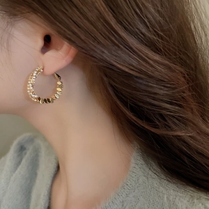 Detail shot of golden C-shaped hoop earrings featuring a twisted texture and inset zircons