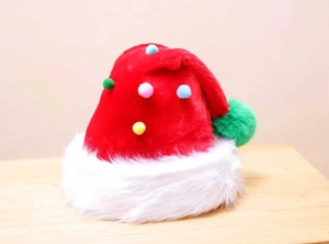 Detail of a red plush Christmas hat with a large green pompom and colorful fuzzy balls