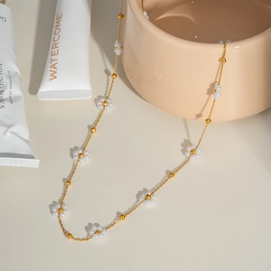 Détail du collier en chaîne dorée avec fleurs en perles blanches sur céramique beige