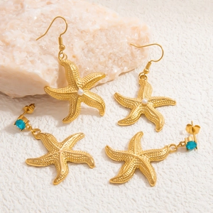Gold starfish drop earrings set with pearls and blue zircons on a textured stone surface