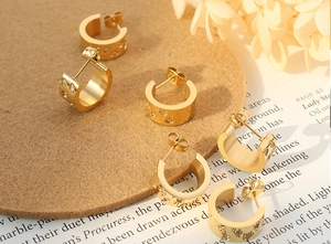 Macro view of gold-plated wide C-shape earrings with inlaid cubic zirconia on felt and book