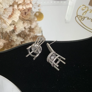Detailed close-up of a silver chair-shaped earring with sparkling cubic zirconia on black velvet