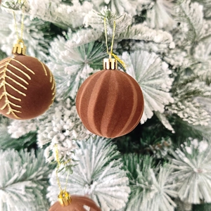 Gros plan de boules de Noël en velours marron avec motifs dorés sur branches enneigées