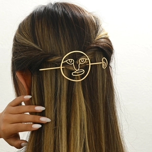 Golden hollow abstract face hair pin made of metal shown on a model's hair