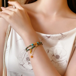 Détail d'un bracelet de perles vertes et oranges avec chaîne dorée au poignet du mannequin