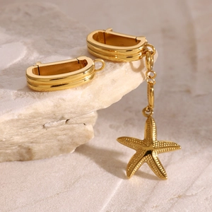 Macro shot of gold U-shaped earrings with starfish charms on natural stone