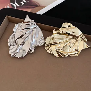 Elegant gold and silver pleated leaf brooches on dark velvet with fashion magazine