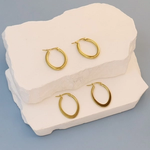 Macro detail of two pairs of gold oval hoop earrings on a textured stone display