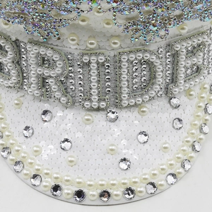 Detailed close-up of white sequined bride hat with pearl BRIDE lettering and rhinestone crown