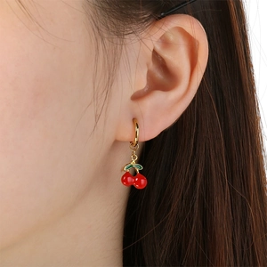 Close-up of a cute red cherry pendant earring with green leaves on a gold hoop