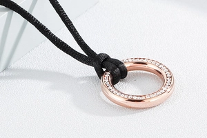 Detailed close-up of rose gold titanium circular pendant with pavé crystals on black cord