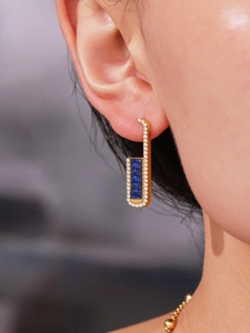 Close-up of golden U-shaped earrings with emerald cut blue stones and sparkling pavé crystals